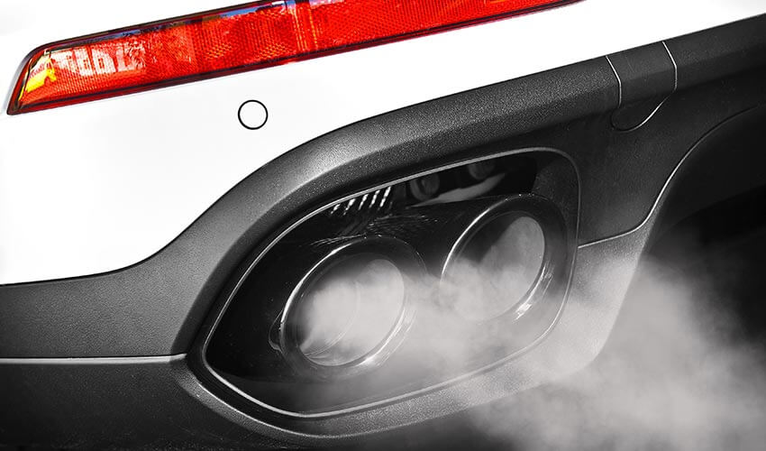 Exhaust pipes on a white car with smoke emitting.
