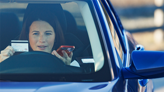 Woman sitting in her parked car on the phone, holding her CAA Membership card